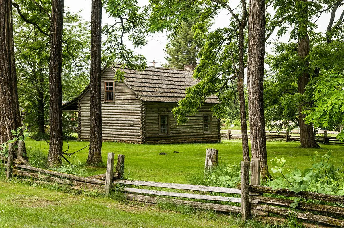 Log cabin surrounded by trees and fence.